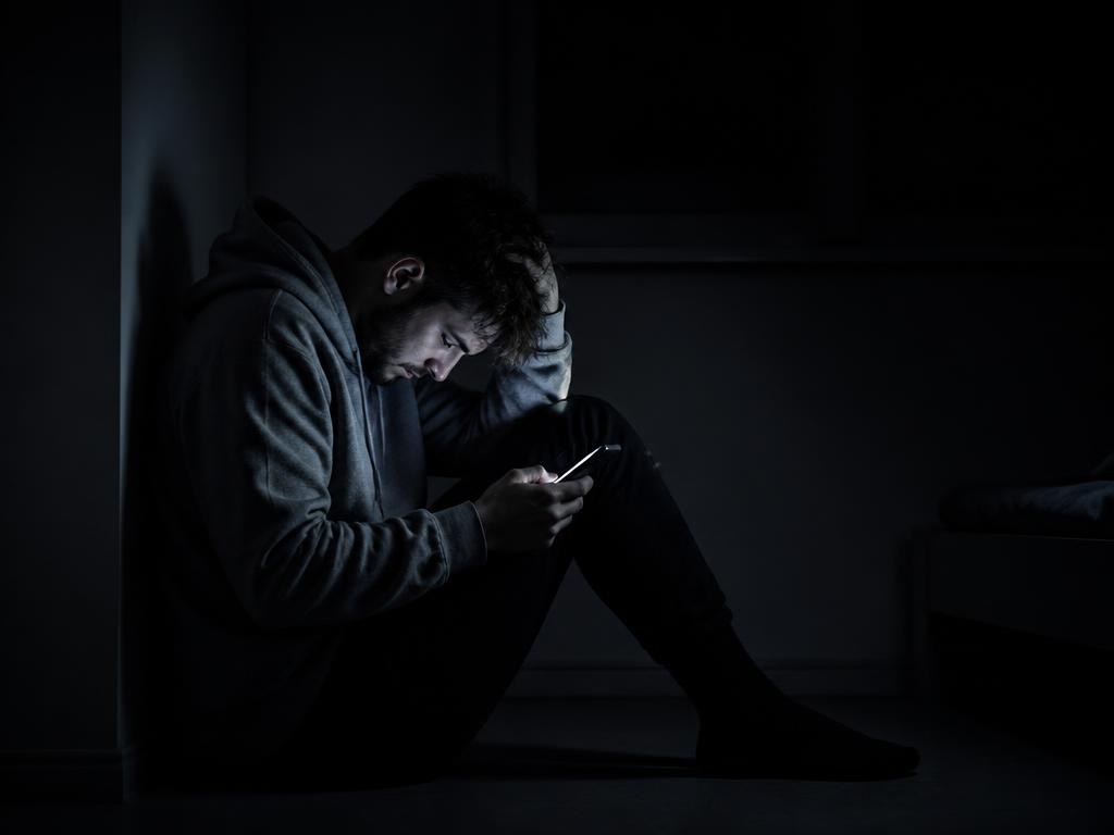Homem sozinho sentado no escuro iluminado pela tela do celular